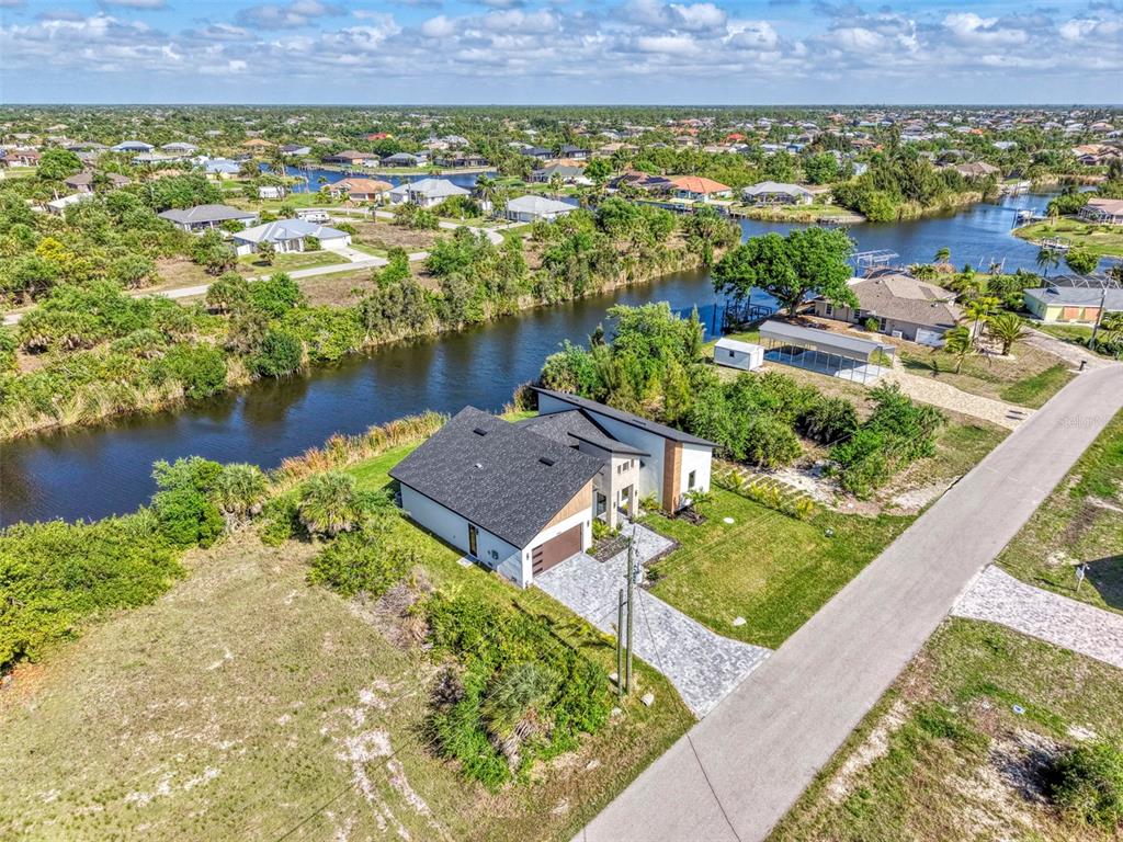 An aerial view shows a modern house with a dark roof situated beside a canal — 9468 ATTICA CIRCLE, PORT CHARLOTTE, FL