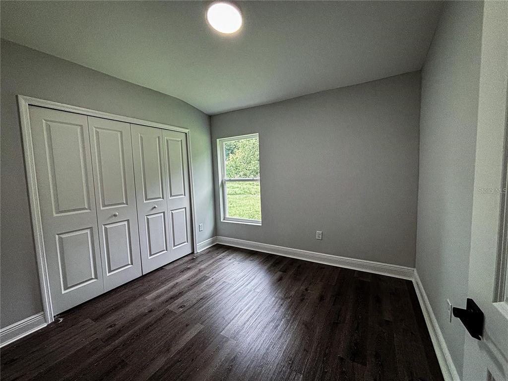A bedroom features gray walls, dark wood-look flooring, a white closet, and a single window — 2855 SE 146TH PLACE, SUMMERFIELD, FL