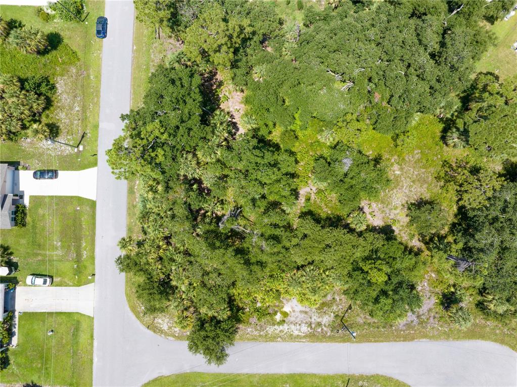 An aerial view shows a wooded, undeveloped corner lot situated between two paved residential streets — POMONA CT, NORTH PORT, FL