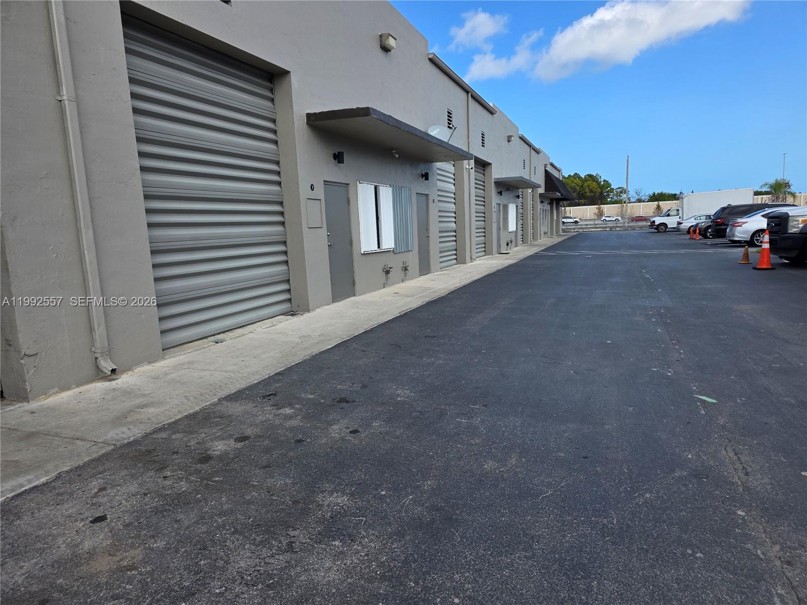 A row of gray industrial warehouse units with roll-up doors and parking spaces — 16225 SW 117th Ave # 6, Miami FL 33177, MIAMI, FL