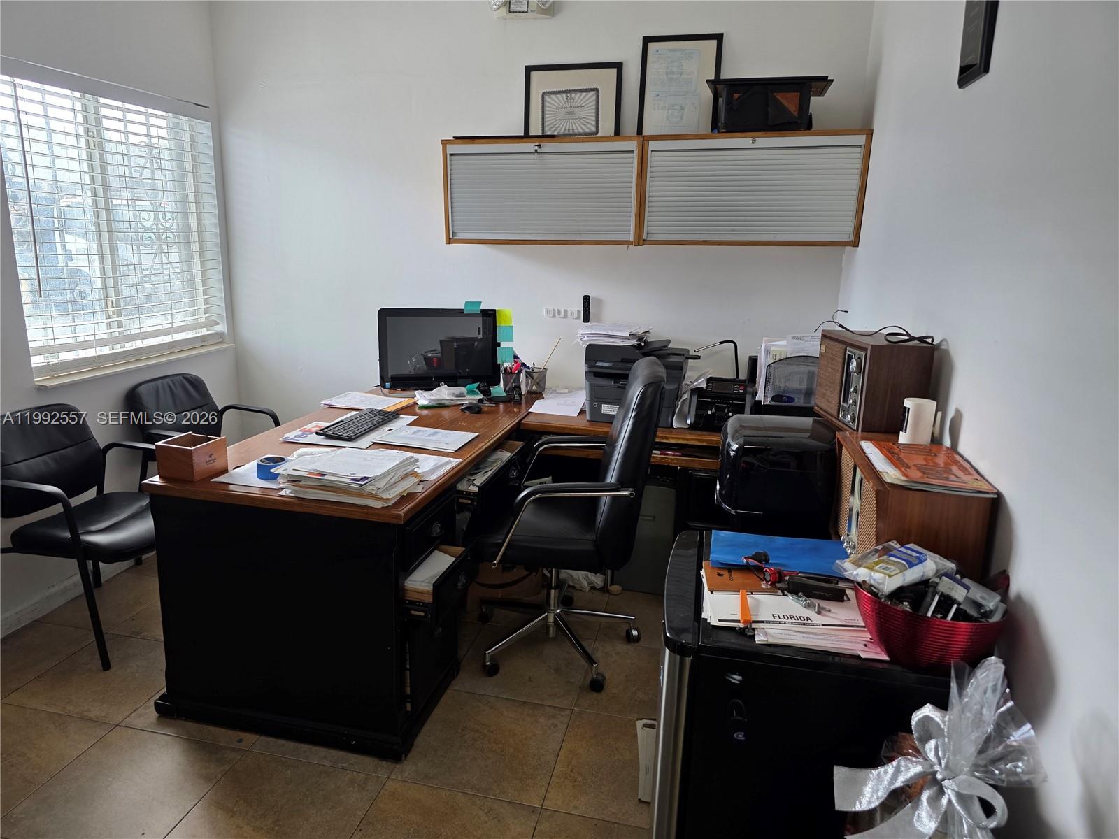 A home office features a wooden desk, black chairs, wall-mounted cabinets, and a window with blinds — 16225 SW 117th Ave # 6, Miami FL 33177, MIAMI, FL