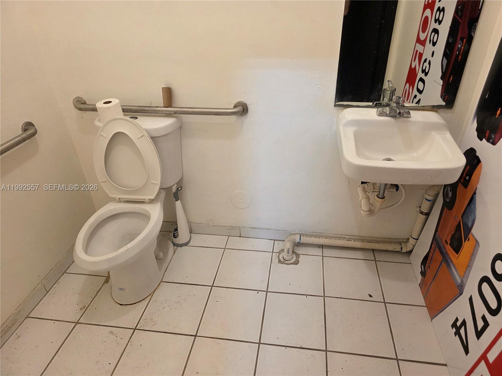 A small, tiled bathroom features a toilet with a grab bar and a wall-mounted sink — 16225 SW 117th Ave # 6, Miami FL 33177, MIAMI, FL