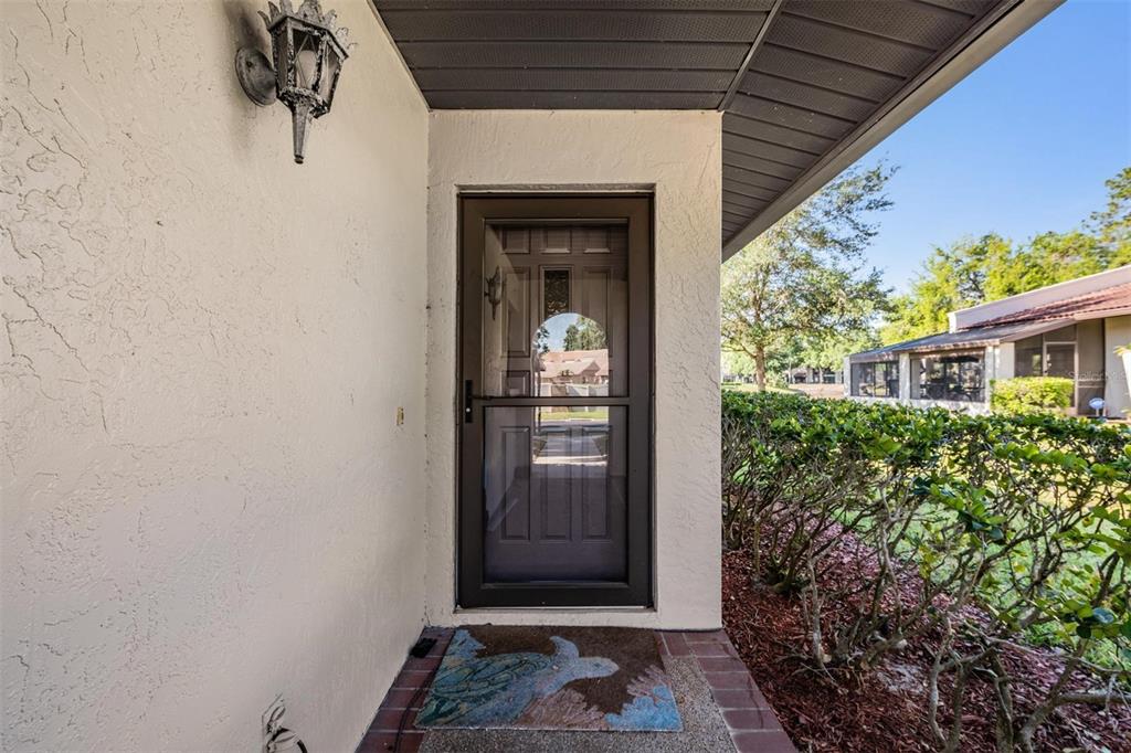 A front entryway features a dark storm door, a wall-mounted lantern, and a patterned doormat — 3505 TARPON WOODS BOULEVARD UNIT N401, PALM HARBOR, FL