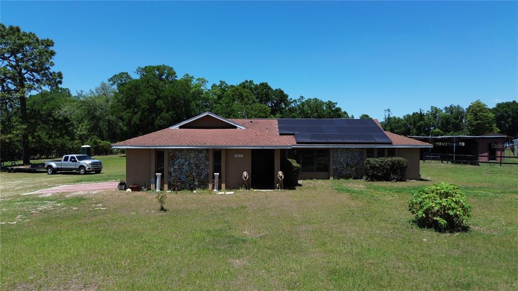 A single-story house with stone accents and solar panels sits on a grassy lot — 10631 W HIGHWAY 40, OCALA, FL