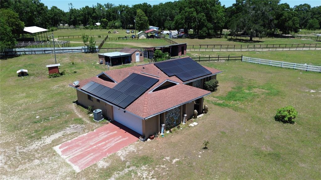 An aerial view shows a house with solar panels on its roof and a fenced yard — 10631 W HIGHWAY 40, OCALA, FL