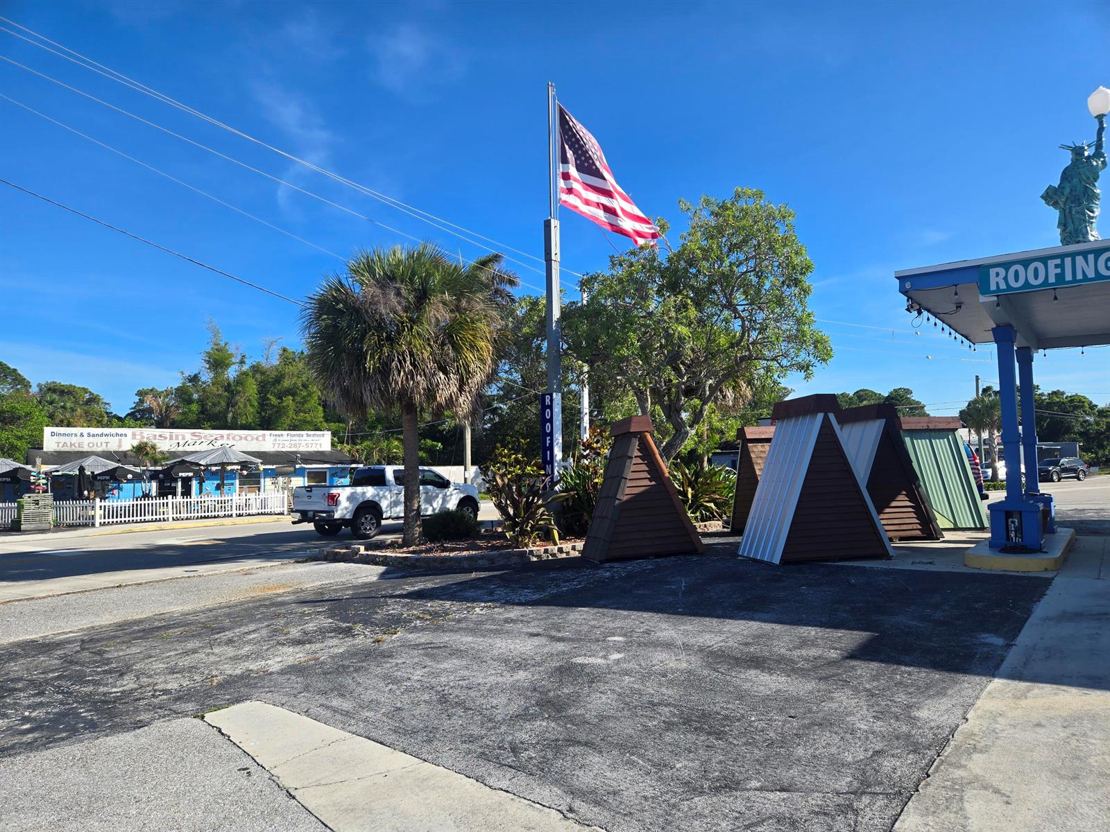 An exterior view of a commercial property featuring a flag, palm tree, and roofing displays — 4149 SE Salerno Road # A, Stuart FL 34997, STUART, FL