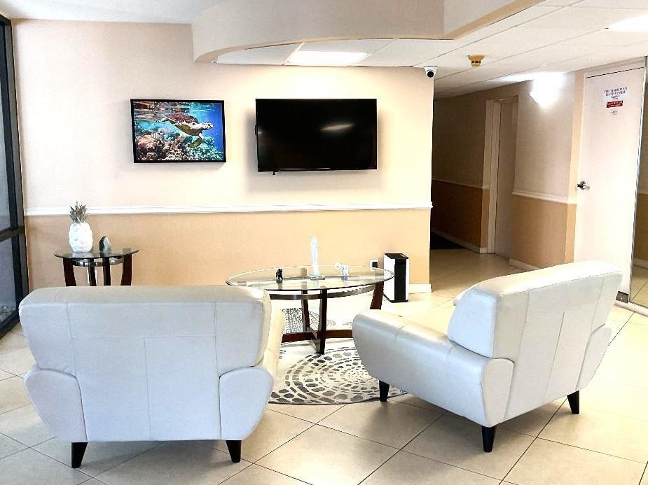 A waiting area features two white armchairs, a glass coffee table, and a wall-mounted television — 777 S Federal Highway, Pompano Beach FL 33062, POMPANO BEACH, FL