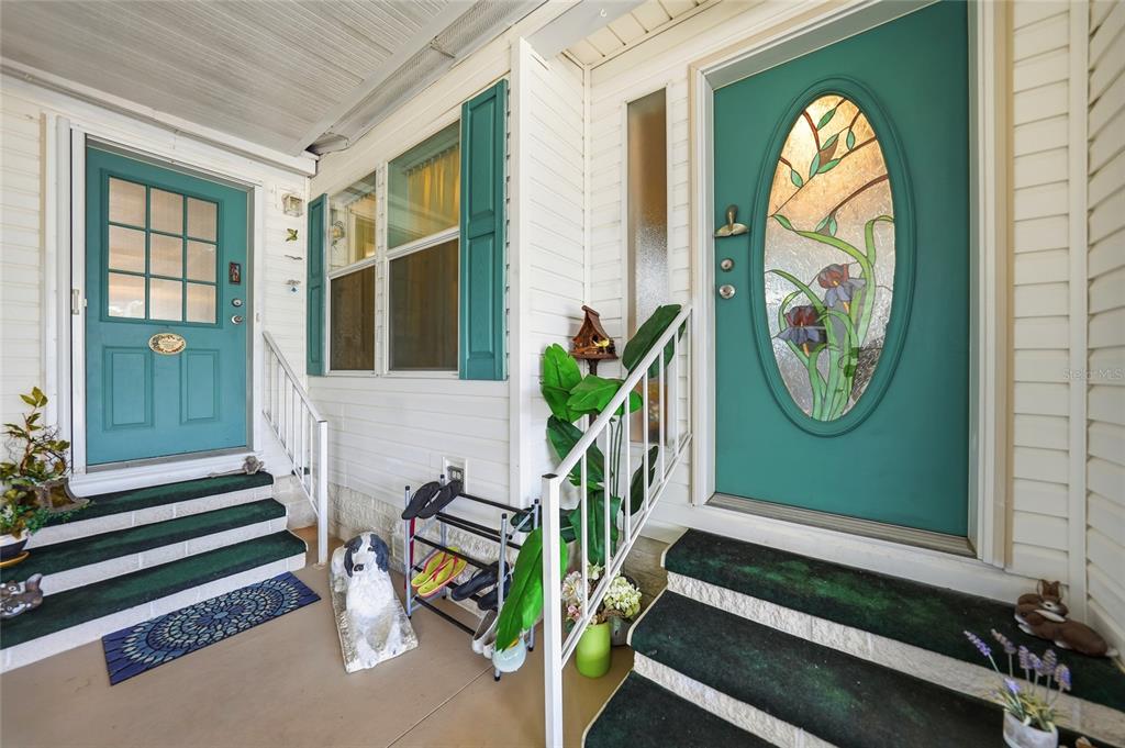 A covered porch features two teal doors, white railings, and steps with green carpet — 600 WOODWYN COURT, NORTH PORT, FL