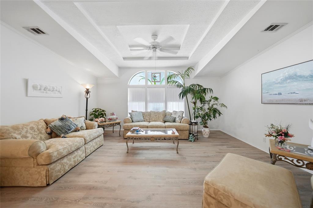 A living room features a tray ceiling, light wood-look flooring, two sofas, and a large window — 600 WOODWYN COURT, NORTH PORT, FL