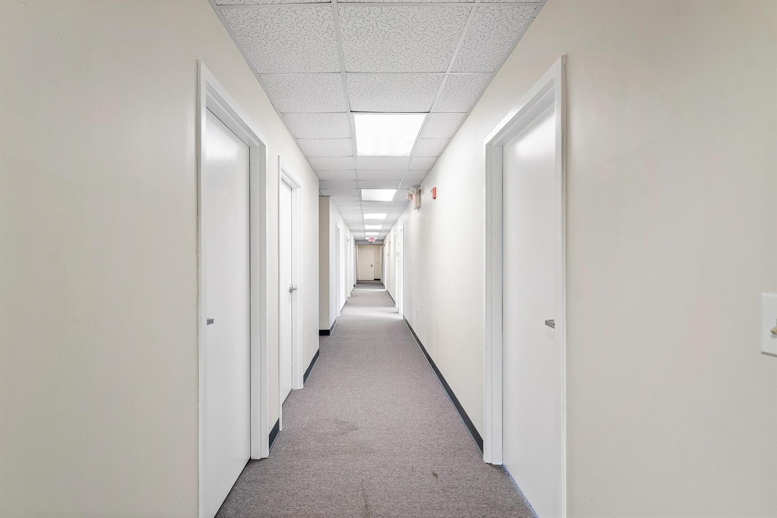 A long, narrow office hallway features white walls, gray carpeting, and a drop ceiling — 555 SW 12th Avenue, Pompano Beach FL 33069, POMPANO BEACH, FL