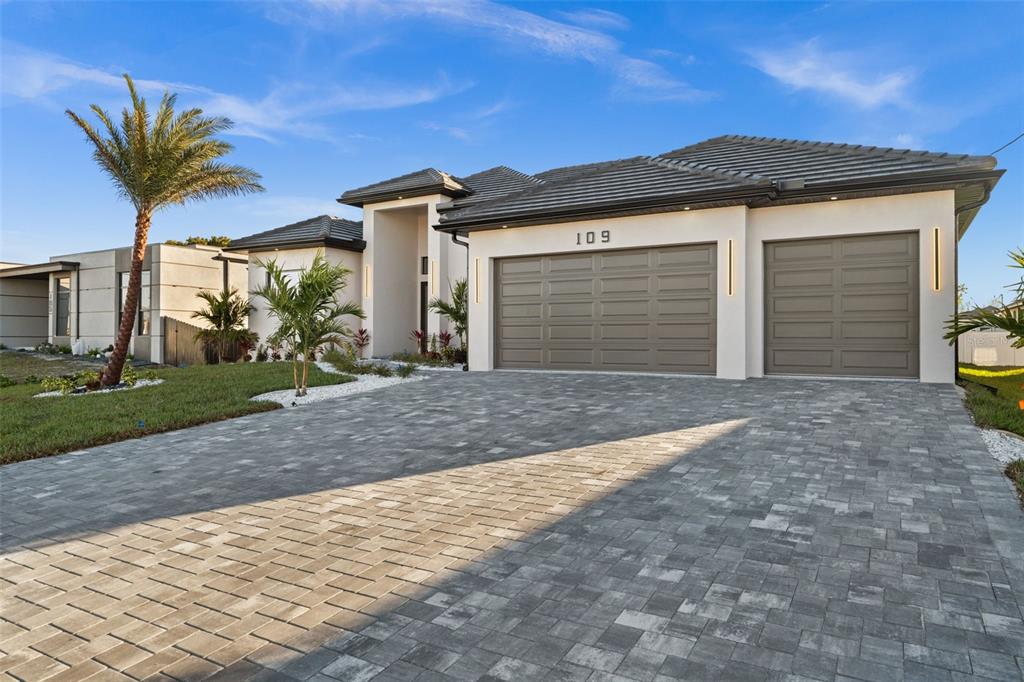 A modern single-story house with a paver driveway, two garage doors, and a palm tree — 109 SW 37TH PLACE, CAPE CORAL, FL