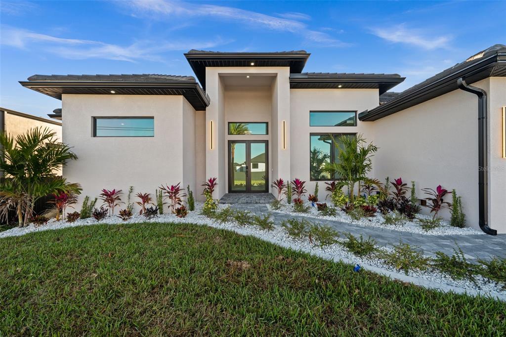 A modern single-story house with a beige stucco exterior, dark trim, and a paved walkway — 109 SW 37TH PLACE, CAPE CORAL, FL