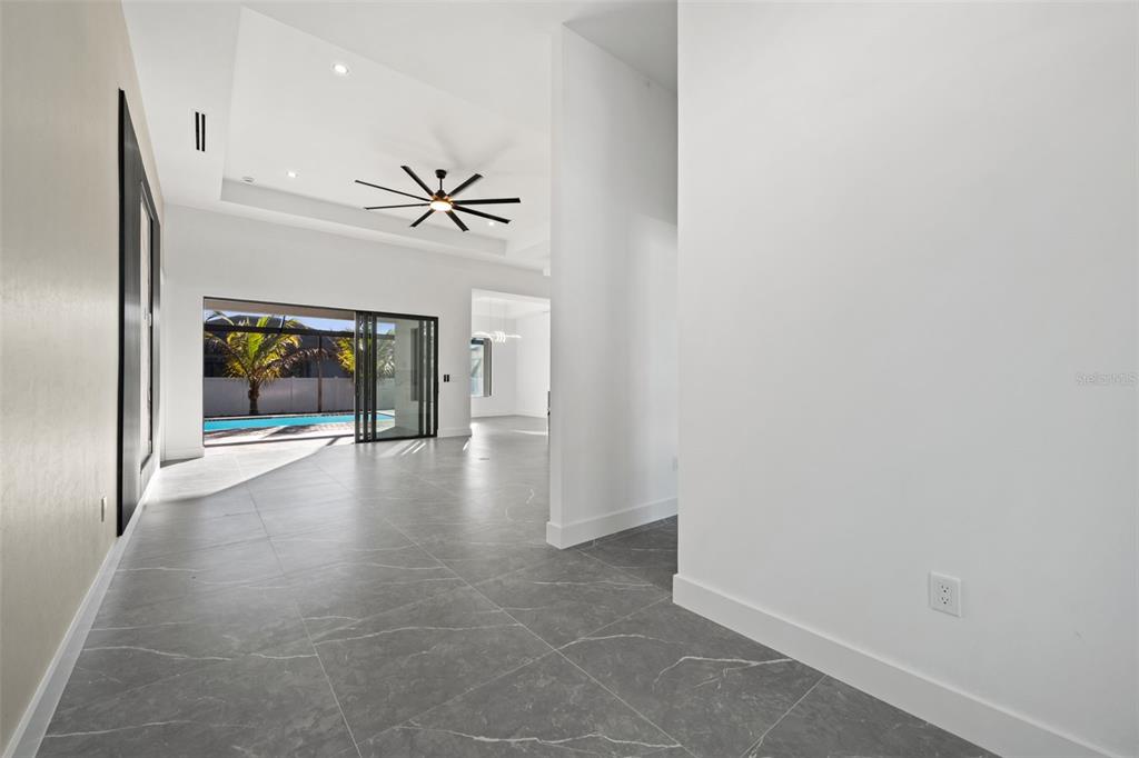 A bright, open-concept living area features gray tile flooring, a tray ceiling, and sliding doors — 109 SW 37TH PLACE, CAPE CORAL, FL