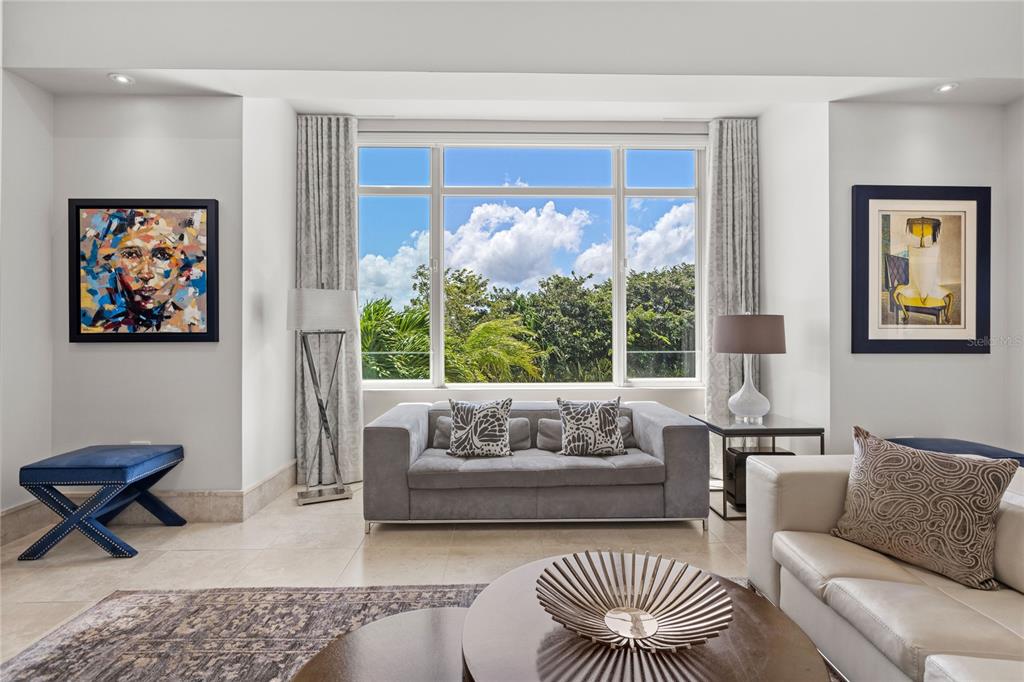 A bright living room features a large window, a grey sofa, and two framed artworks — 500 PLANTATION DRIVE UNIT 3-202, DORADO, PR