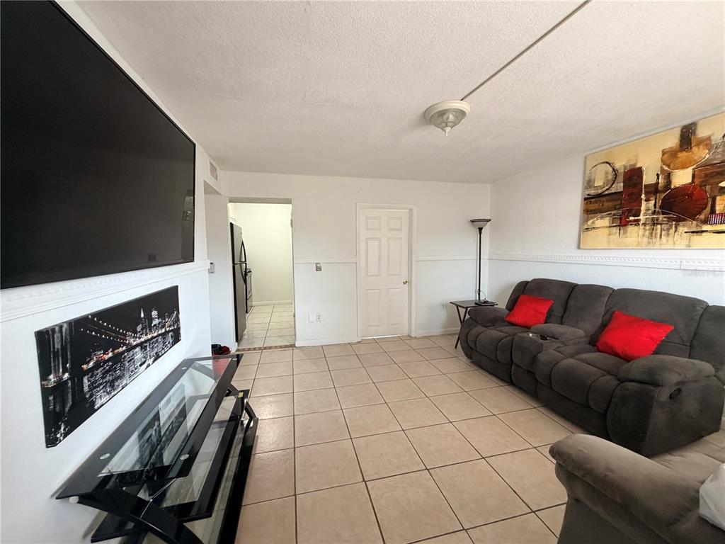 A living room features tile flooring, a large wall-mounted television, and a dark grey sofa — 738 RIDENHOUR CIRCLE UNIT L, ORLANDO, FL