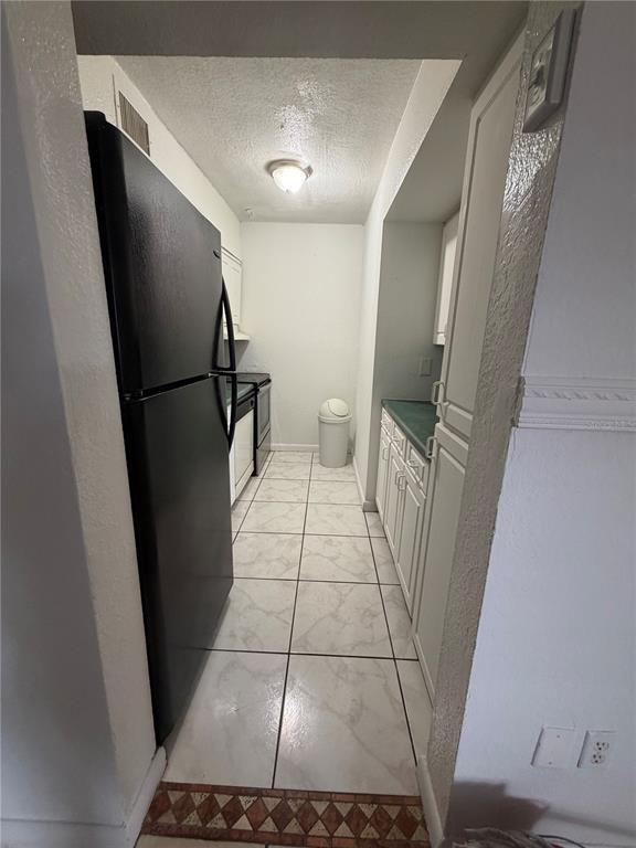 A narrow kitchen features white cabinets, a black refrigerator, and light-colored tiled flooring — 738 RIDENHOUR CIRCLE UNIT L, ORLANDO, FL