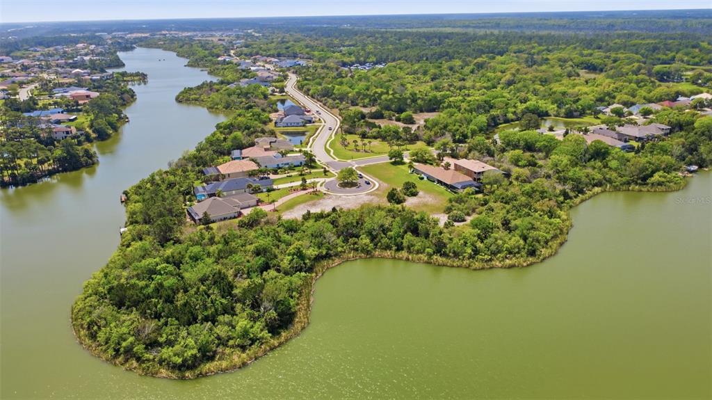 An aerial view shows a residential neighborhood situated on a peninsula surrounded by a lake — 151 N LAKEWALK DRIVE, PALM COAST, FL