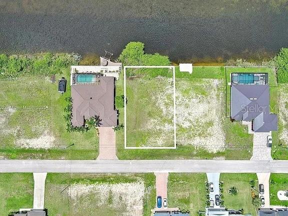 An aerial view shows a vacant waterfront lot situated between two existing residential properties — 401 NW 24TH TERRACE, CAPE CORAL, FL