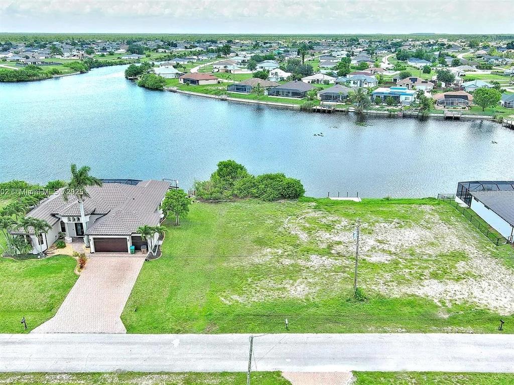 An aerial view shows a vacant waterfront lot situated next to a single-family home — 401 NW 24TH TERRACE, CAPE CORAL, FL