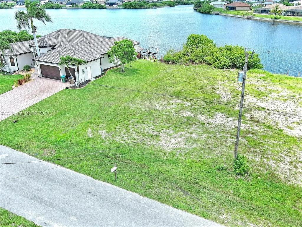 An aerial view shows a vacant grassy lot next to a house by a canal — 401 NW 24TH TERRACE, CAPE CORAL, FL