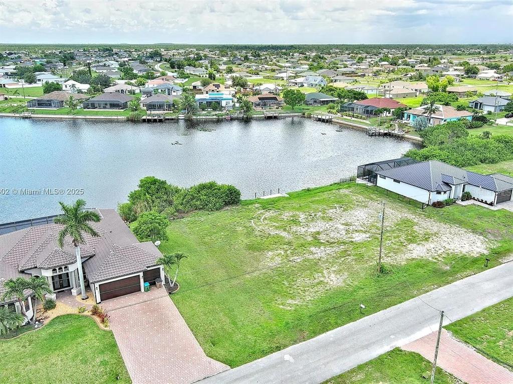 An aerial view shows a vacant waterfront lot situated between two residential houses — 401 NW 24TH TERRACE, CAPE CORAL, FL