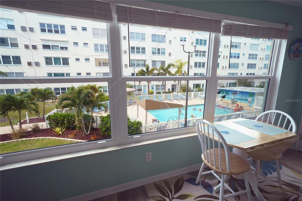 A dining area with a table and chairs overlooks a swimming pool and apartment buildings — 2960 59TH STREET S UNIT 210, GULFPORT, FL