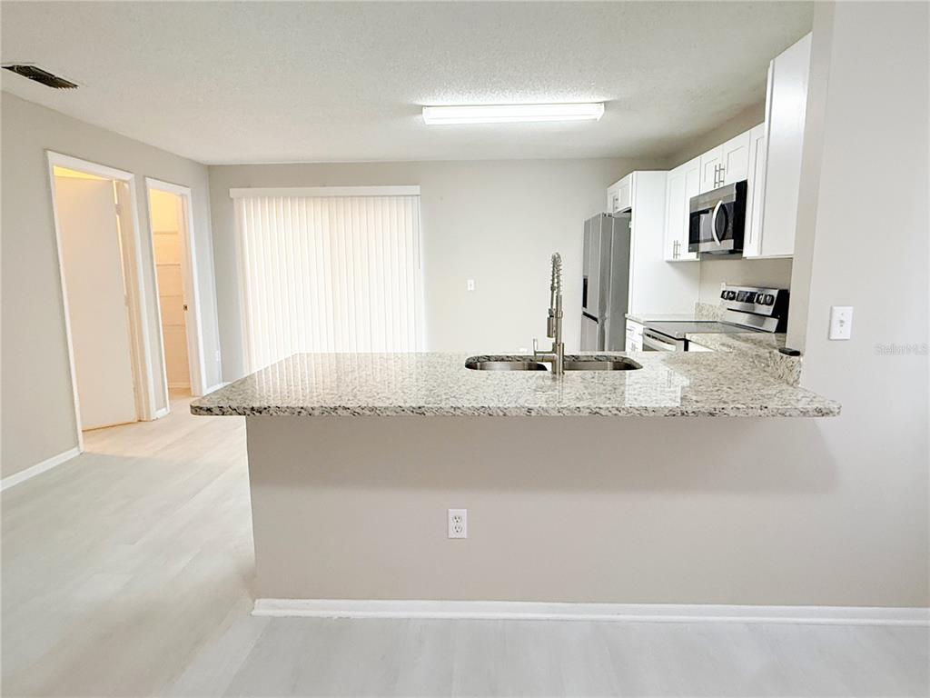 A kitchen with a granite-topped island, white cabinets, and stainless steel appliances — 4417 RIBBLESDALE LANE, ORLANDO, FL