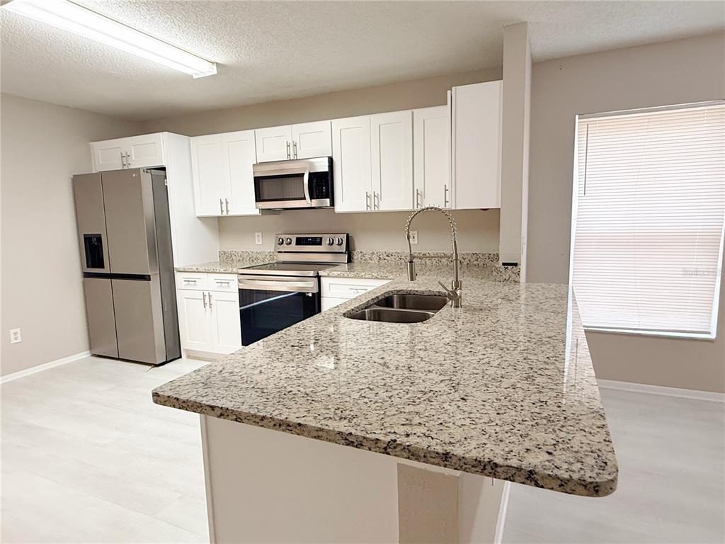 A kitchen features white cabinets, stainless steel appliances, and a granite-topped island with a sink — 4417 RIBBLESDALE LANE, ORLANDO, FL