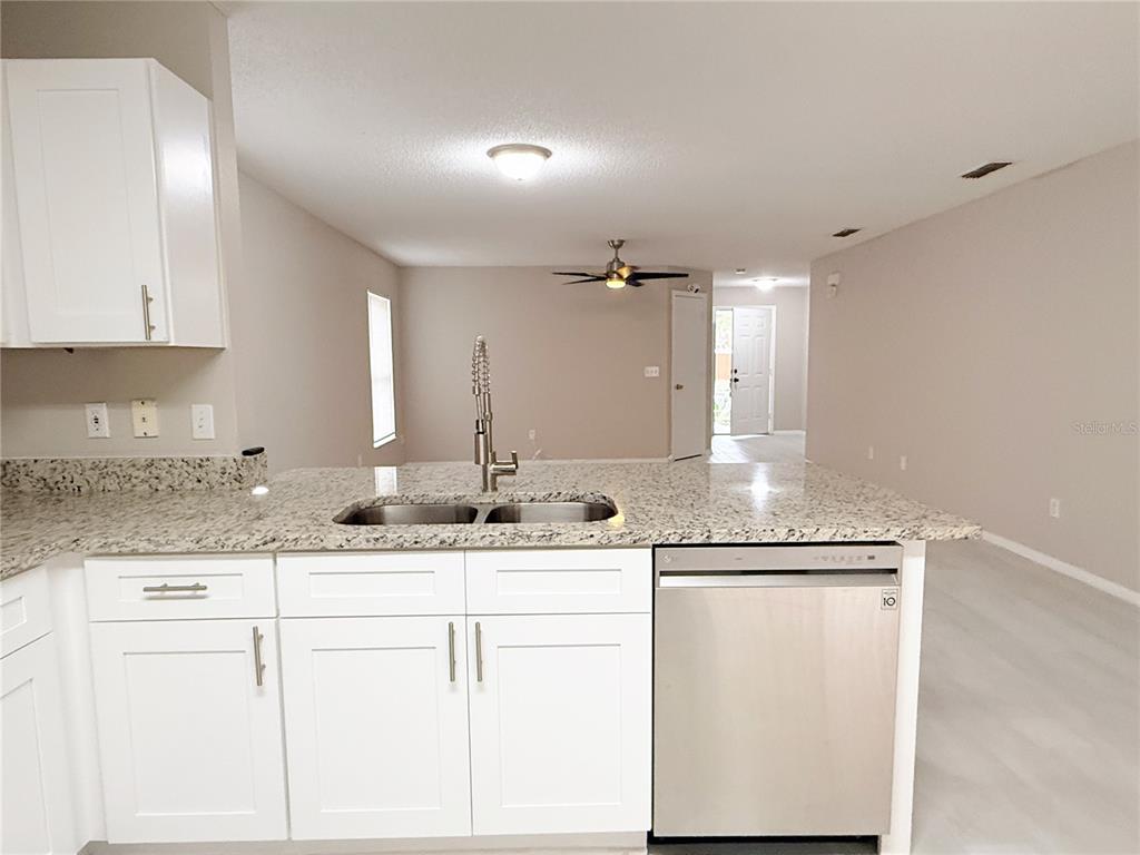 A kitchen with white cabinets, granite countertops, and a stainless steel dishwasher overlooks a living area — 4417 RIBBLESDALE LANE, ORLANDO, FL