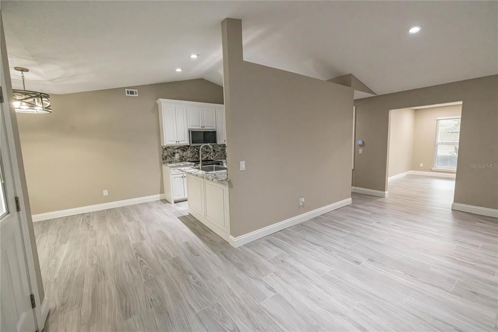 A kitchen with white cabinets and granite countertops overlooks a living area with wood-look flooring — 6178 SWAINSON STREET, MILTON, FL