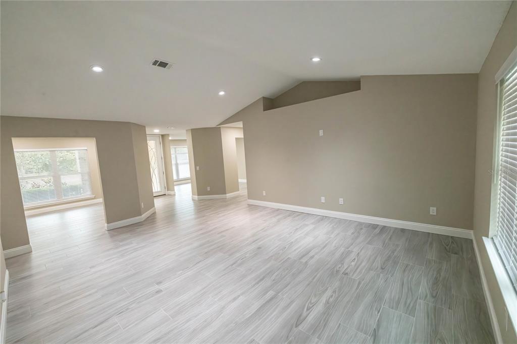 An empty living room features light gray wood-look tile flooring, beige walls, and a vaulted ceiling — 6178 SWAINSON STREET, MILTON, FL