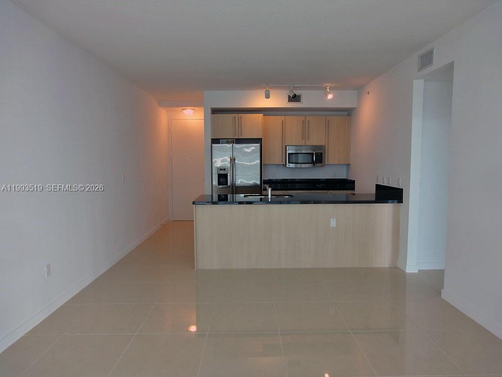 A kitchen with light wood cabinets, black countertops, and stainless steel appliances opens to a room — 1111 SW 1 AV, Miami FL 33130, MIAMI, FL