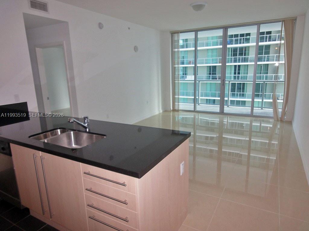 A kitchen island with a black countertop and sink overlooks an empty living area — 1111 SW 1 AV, Miami FL 33130, MIAMI, FL