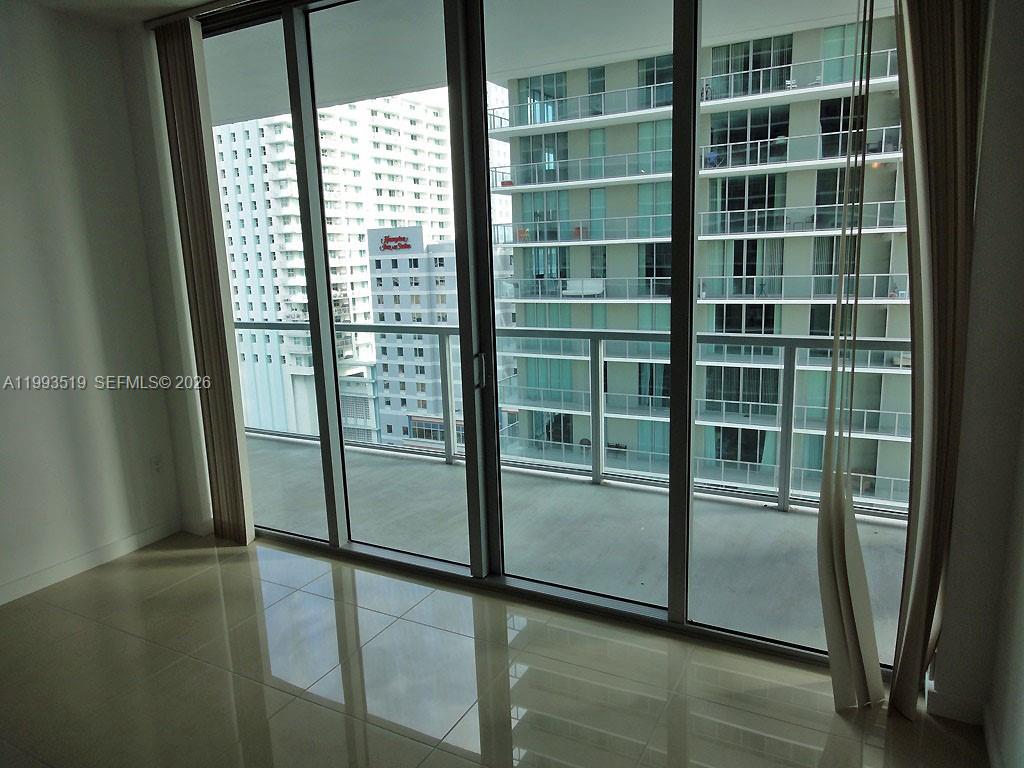 A room with light-colored tile flooring features a large sliding glass door leading to a balcony — 1111 SW 1 AV, Miami FL 33130, MIAMI, FL