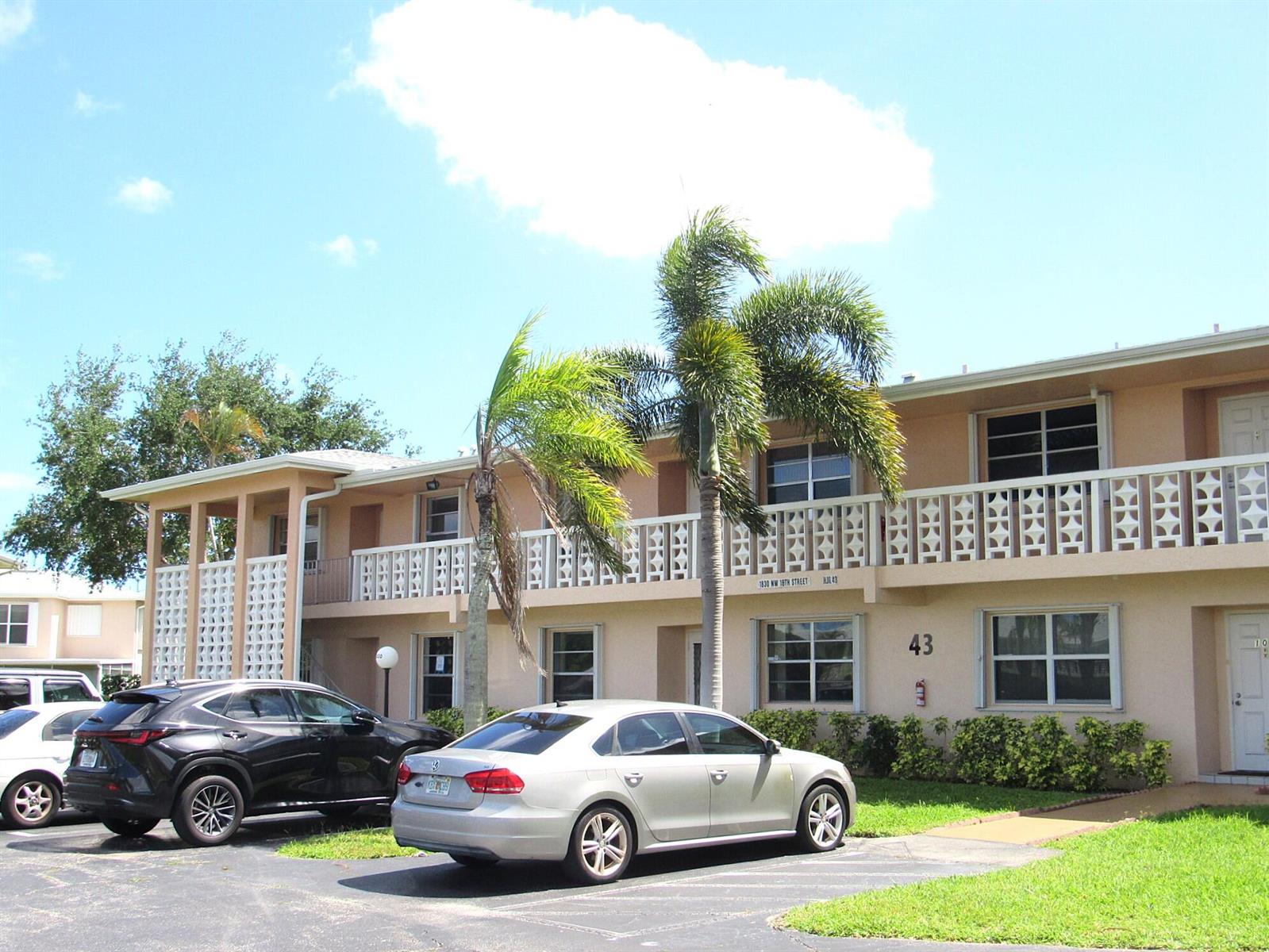 A two-story apartment building with a white balcony railing, palm trees, and parked cars — 1830 NW 18th Street # 201, Delray Beach FL 33445, DELRAY BEACH, FL