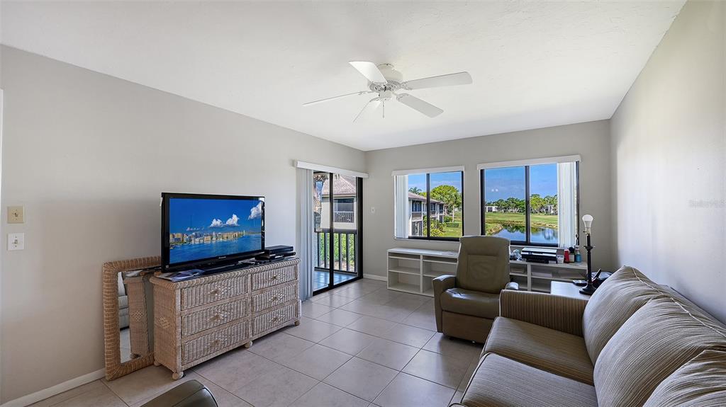 A tiled sunroom features large sliding glass doors overlooking a lake and golf course — 5207 WILLOW LINKS UNIT 34, SARASOTA, FL