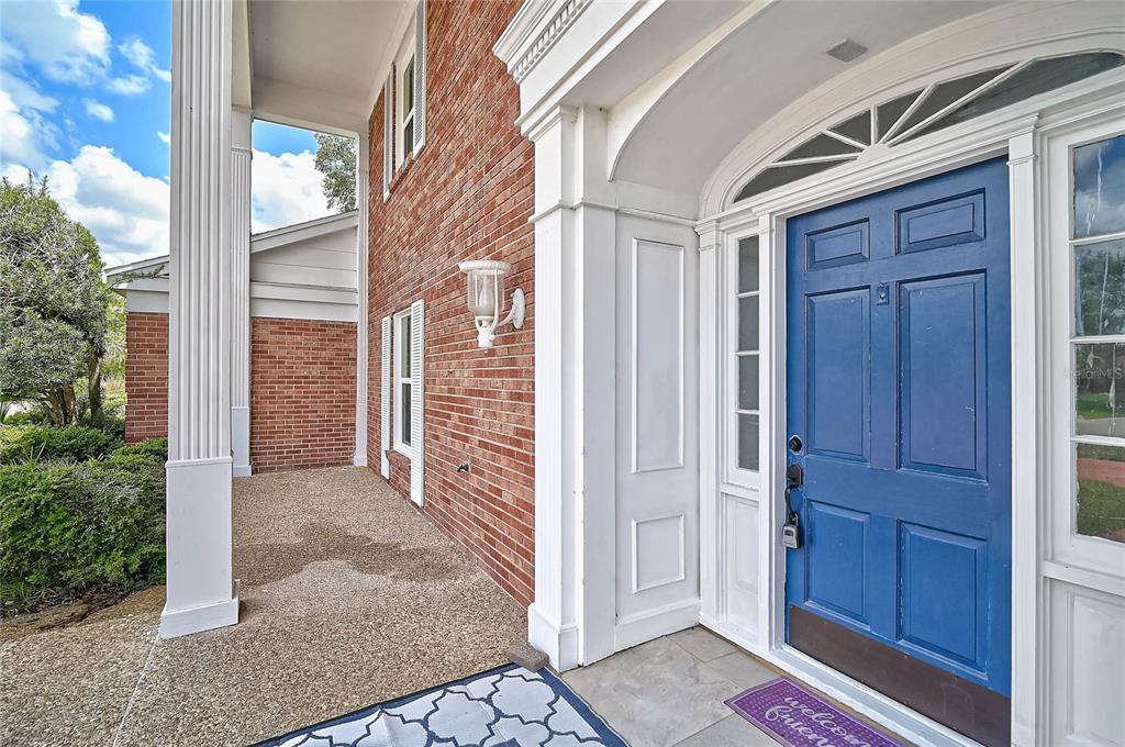 A blue front door with sidelights sits under a covered porch with brick walls — 3215 PINE VALLEY DRIVE, SARASOTA, FL