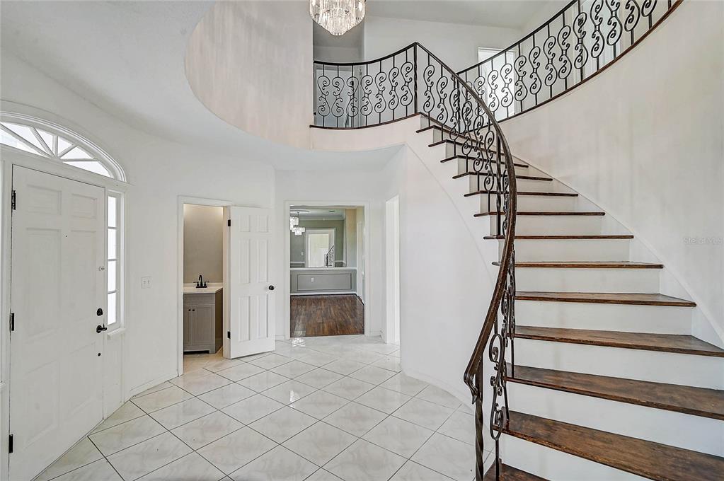 A foyer features white tile flooring, a curved staircase with iron railings, and a chandelier — 3215 PINE VALLEY DRIVE, SARASOTA, FL
