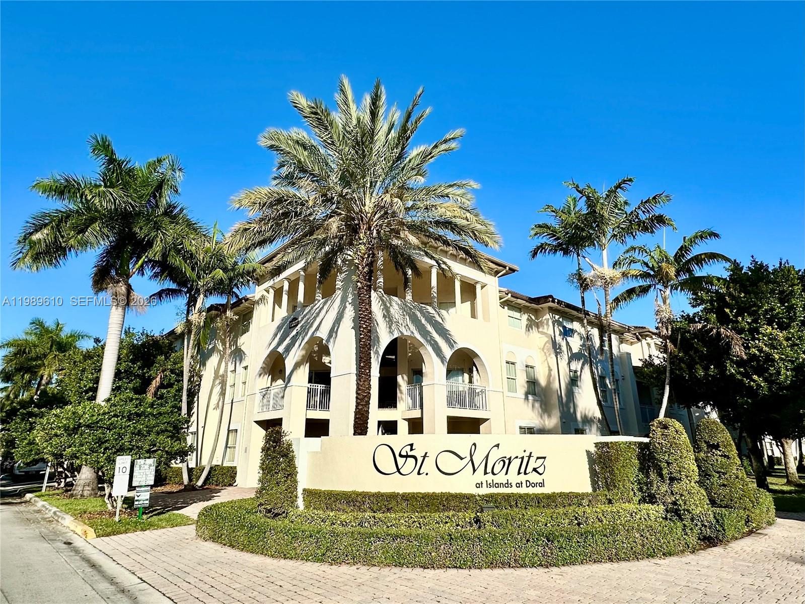 The exterior of a multi-story apartment building features arched balconies and a prominent community sign — 11403 NW 89th St # 219, Doral FL 33178, DORAL, FL