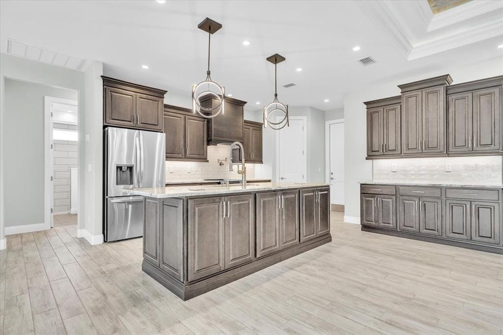 A kitchen features dark wood cabinets, a large central island, and light-colored wood-look flooring — 26251 COPIAPO CIRCLE, PUNTA GORDA, FL