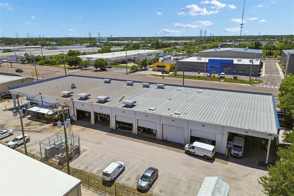 An aerial view shows a long industrial warehouse building with multiple roll-up doors and parking — 9945 RACE TRACK ROAD, TAMPA, FL
