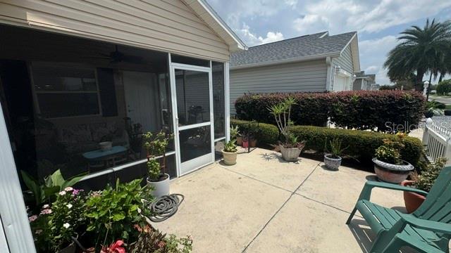 A screened-in patio with a concrete floor, potted plants, and a green chair outside — 2029 FAIRVIEW LANE, THE VILLAGES, FL