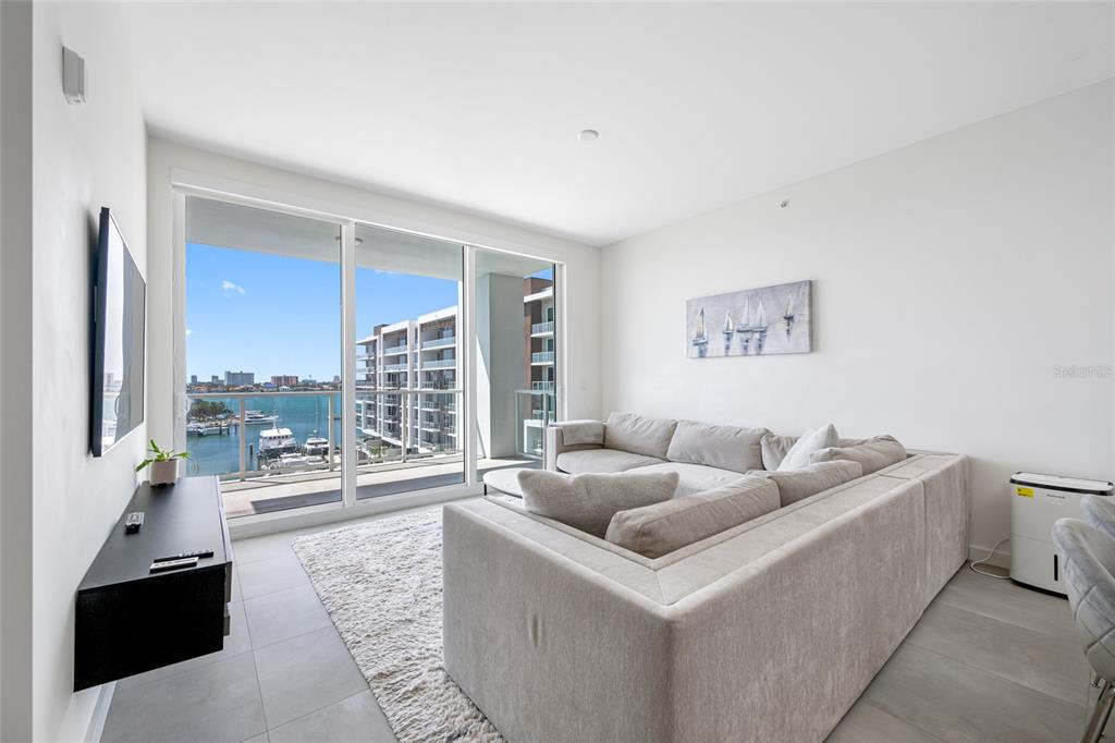 A living room features a large sectional sofa, a wall-mounted television, and a balcony view — 900 N OSCEOLA UNIT 603, CLEARWATER, FL