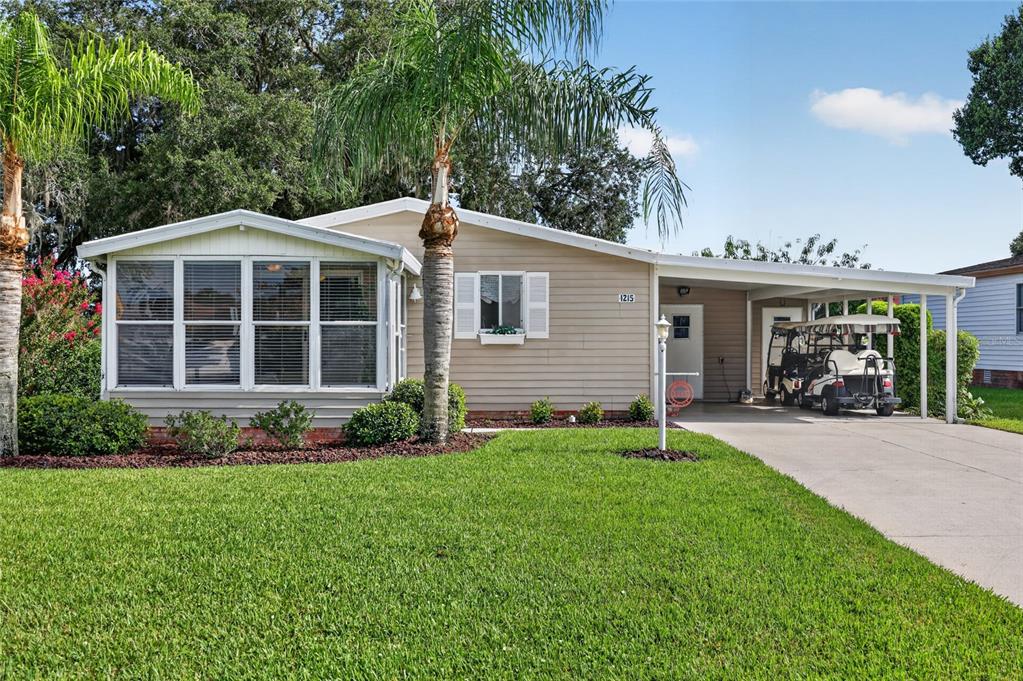 A single-story house with tan siding, a sunroom, a carport, and a golf cart parked outside — 1215 PANAMA PLACE, THE VILLAGES, FL