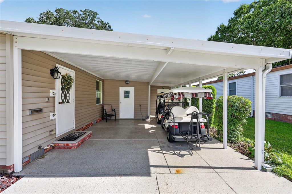 A concrete carport with a golf cart sits beside a house with tan siding — 1215 PANAMA PLACE, THE VILLAGES, FL