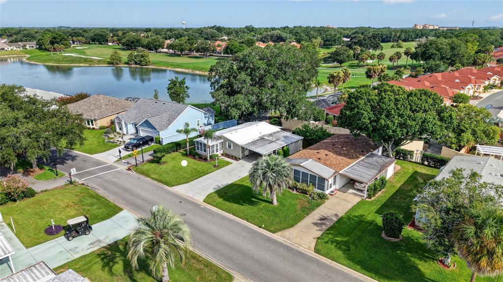 An aerial view shows several single-story houses with driveways and lawns near a lake — 1215 PANAMA PLACE, THE VILLAGES, FL