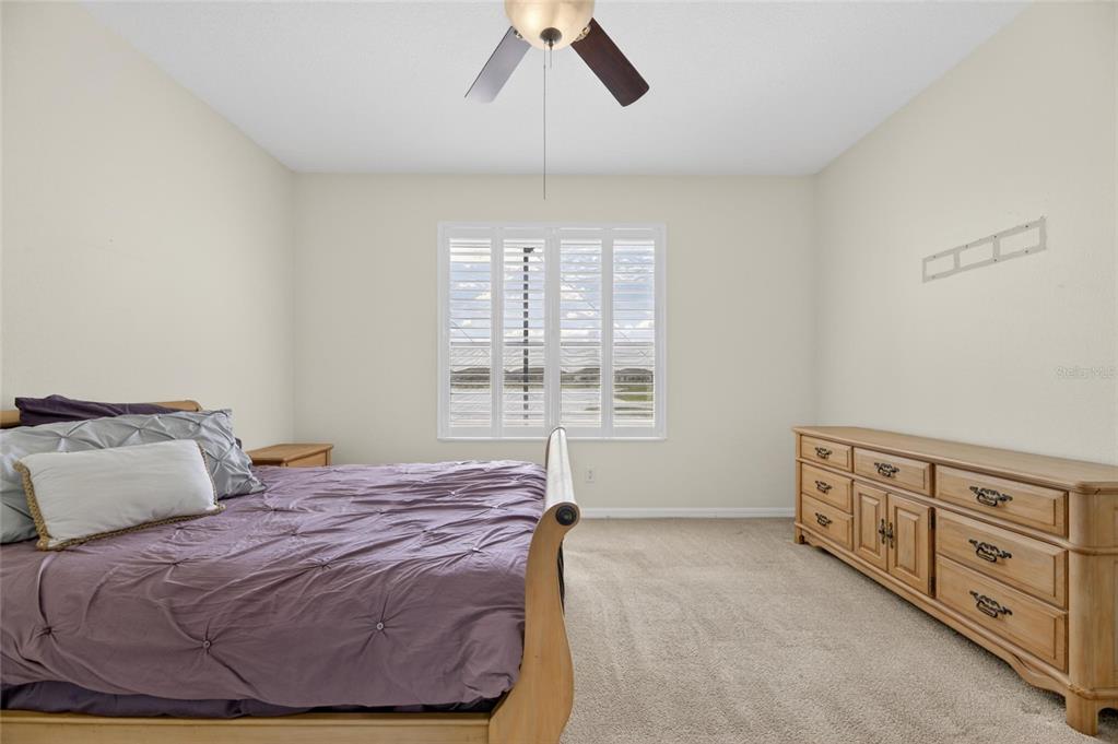 A bedroom features a bed with a purple comforter, a wooden dresser, and plantation shutters — 5667 SUNSET FALLS DRIVE, APOLLO BEACH, FL