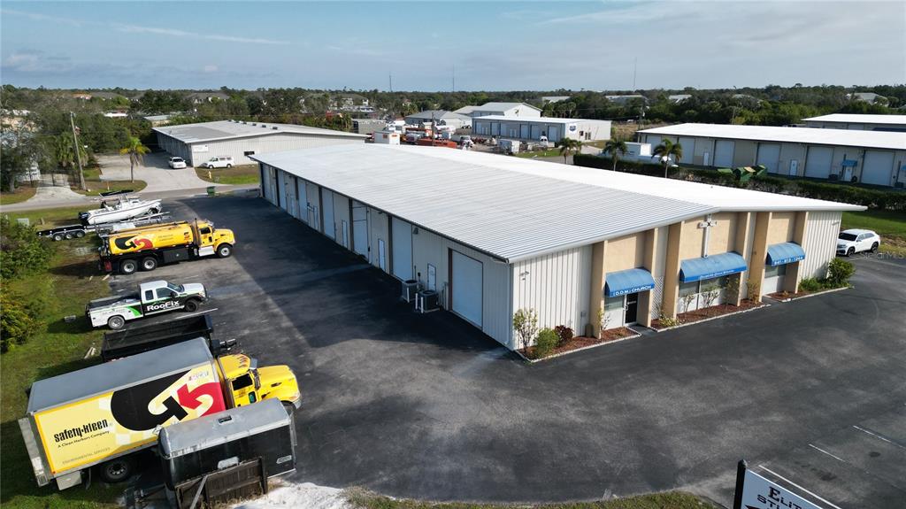 An aerial view shows a long, metal-sided commercial warehouse building with a paved parking lot — 23375 JANICE AVENUE UNIT 12, PUNTA GORDA, FL