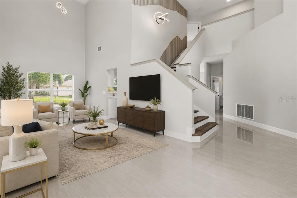 A bright living room features high ceilings, a staircase, and a television on a console — 1005 CHASE DRIVE, WINTER GARDEN, FL