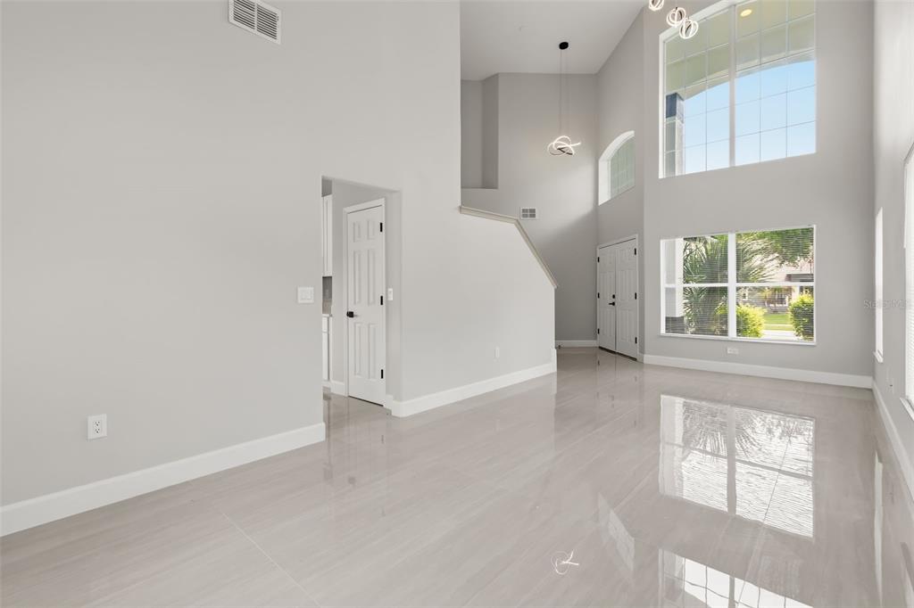 A bright, open-concept living area features high ceilings, large windows, and light-colored tile flooring — 1005 CHASE DRIVE, WINTER GARDEN, FL